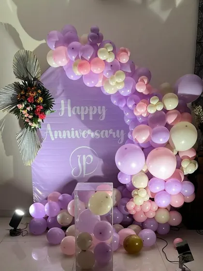 An anniversary decoration featuring a custom purple backdrop and a balloon arch in shades of lavender, pink, and cream. This setup is ideal for an elegant at-home celebration.