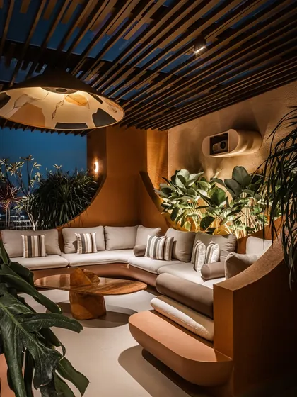 The curved planter wall, filled with lush monstera and other foliage, is uplit to create a dramatic backdrop for the main seating area. This technique adds depth and a sense of enclosure to the outdoor room.