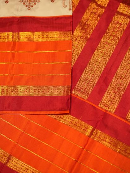 The vibrant, multi-banded red and orange pallu provides a stunning contrast to the serene white body and its delicate embroidery.