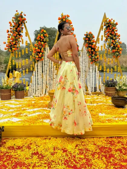 A playful look over the shoulder, showing the back of the Haldi outfit and the beautiful floral stage decor.
