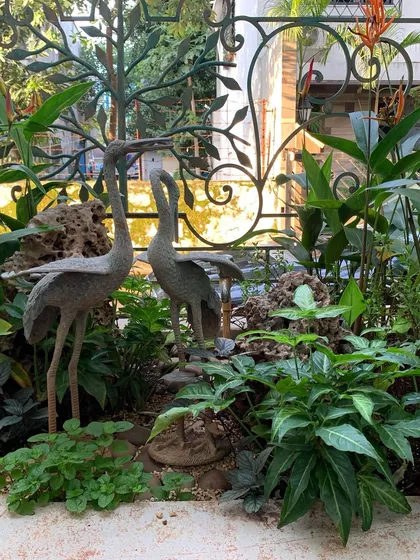 A pair of elegant crane sculptures stand amidst a bed of green foliage, adding an artistic touch to this garden corner.