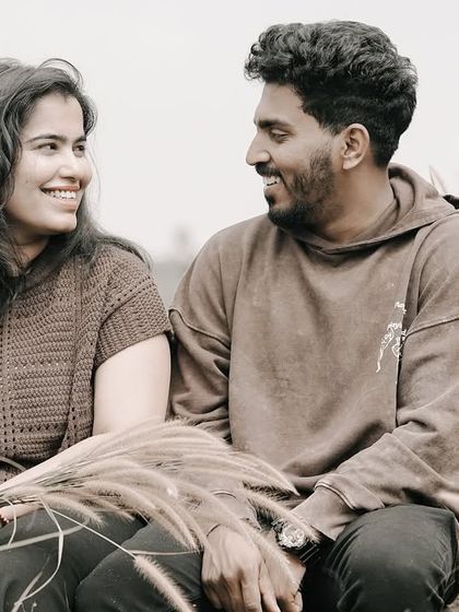 A smiling portrait of a couple sitting in a field of tall grass, capturing a natural and relaxed interaction.