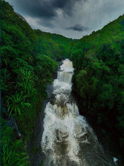 A wide, powerful waterfall in Meghalaya seen from above, with dark, stormy clouds gathering overhead, perfectly capturing the dramatic mood of the monsoon.