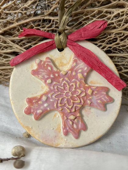 A beautiful pink snowflake ornament, ready to hang on the tree. The textured details and soft color make it a delicate and unique addition to any holiday decor.
