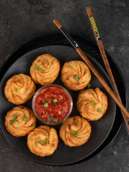 Fried momos styled with a spicy dipping sauce for Momos Corner. The dark background makes the golden-brown momos stand out.