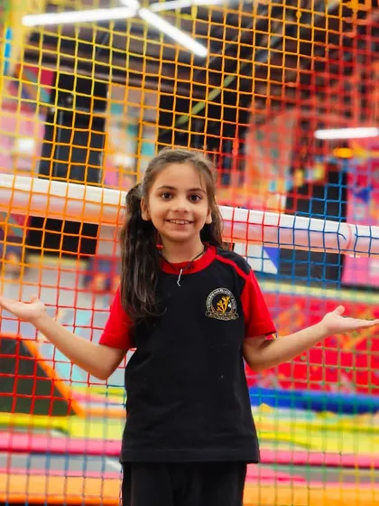 A student welcomes you to her playground, with the colorful and exciting park visible behind her.