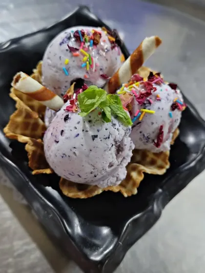 Our seasonal Fresh Jamun Ice Cream. Made with real jamun fruit, this ice cream has a beautiful color and a unique sweet and tart flavor, served in a waffle cone bowl.