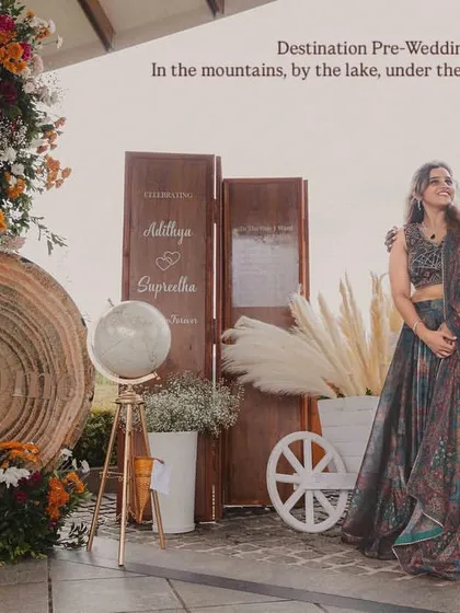 A beautiful shot of the couple at their destination pre-wedding celebration in Wayanad. The rustic decor, including the welcome sign and globe, reflects the natural beauty of the surroundings.