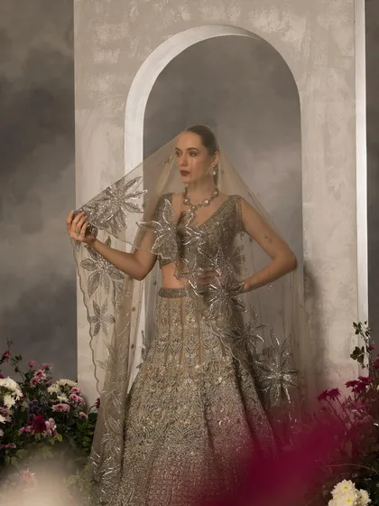 This image showcases a heavily embellished silver-grey lehenga, with the model holding a sheer, star-embroidered dupatta. The styling creates a dreamy, celestial mood, perfect for a modern bride looking for something unique.