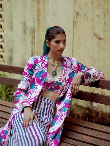 A vibrant street fashion look. The colorful, patterned outfit pops against the neutral background of the bench and wall.