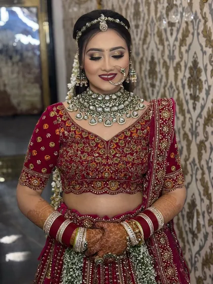Elegance in a deep red lehenga. This bride's look is accentuated with soft, glowing makeup and a bold red lip, perfectly complementing her intricate polki and emerald jewellery.