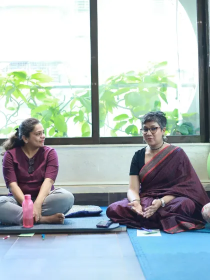 Two women engaged in conversation, seated comfortably on the floor, showing the informal and supportive nature of the gathering.