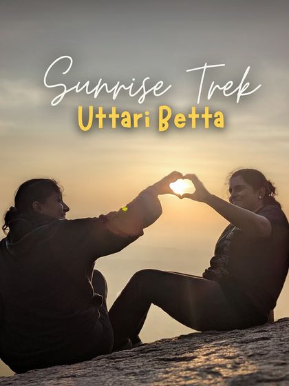 Two friends make a heart shape with their hands around the rising sun, a perfect memory from our Uttari Betta trek.