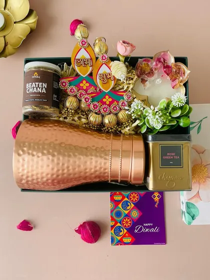 This hamper, in a dark green box with a floral lid, is a premium choice. It features a hammered copper bottle, decorative hangings, rose green tea, and snacks.