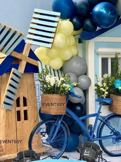A detailed view of the wooden windmill prop and the blue bicycle with baskets of fresh flowers.