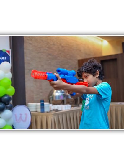 A young guest takes aim with a toy gun at a shooting gallery. I provide a variety of safe shooting games, like Nerf or water gun challenges, to match your party's theme.