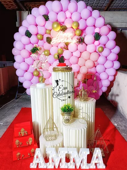 An elegant birthday setup for 'Amma' with a dense pink balloon wall. The plinths and marquee letters add a touch of sophistication.
