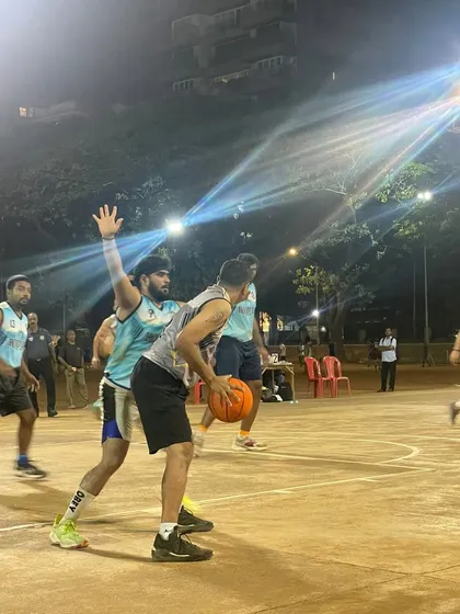 A men's league player drives to the basket, defended closely by an opponent under the bright court lights.