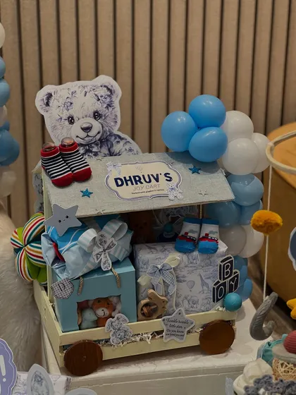 A closer look at 'Dhruv's Gadget' hamper. This toy truck is filled with goodies, including tiny socks and clothes, all personalized for the new arrival and decorated with a teddy bear and balloons.