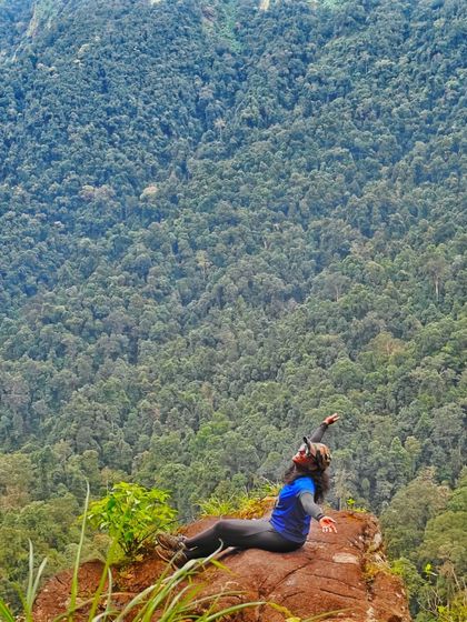 A trekker lies back on a rock, joyfully soaking in the sun and the incredible forest view.