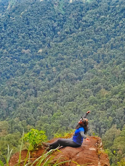 A trekker reclines on a rock, arms outstretched, enjoying the view of the forest below. This is the feeling of freedom and joy our treks provide.