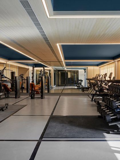 Another view of the gym at 'The Bandra Project', showing the combination of wood-look flooring and mirrored walls. The lighting is integrated into the ceiling design to create a bright and energizing atmosphere.