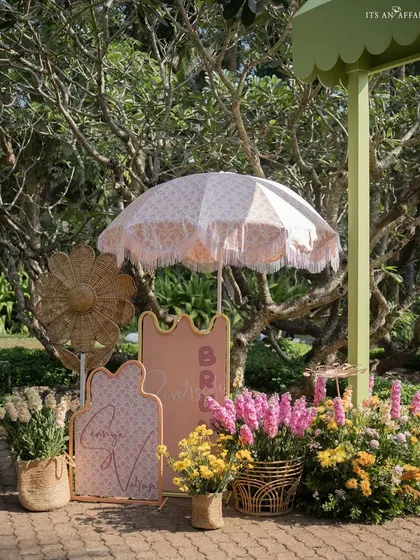 Detailed welcome signage with custom calligraphy, surrounded by flowers and a classic fringed umbrella.