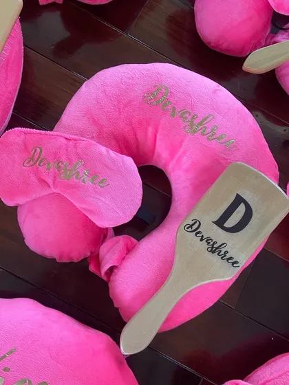 A close-up of the personalized travel favor set, showing the custom name detail on the pillow, eye mask, and hairbrush.