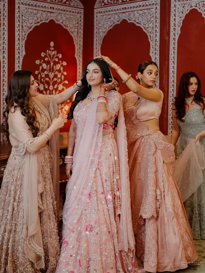 The final touches from her closest friends. I love capturing these candid moments of sisterhood. The coordinated pastel lehengas were chosen to create a soft, harmonious frame around the bride in her beautiful pink ensemble.