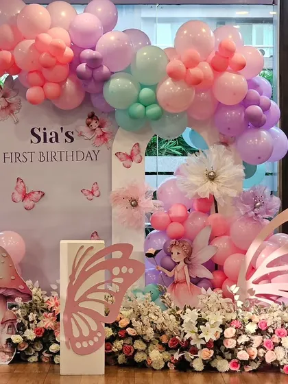 A magical fairy and butterfly theme for Sia's first birthday. The setup includes a custom backdrop, large butterfly wing props, mushroom cutouts, and a pastel balloon arch.