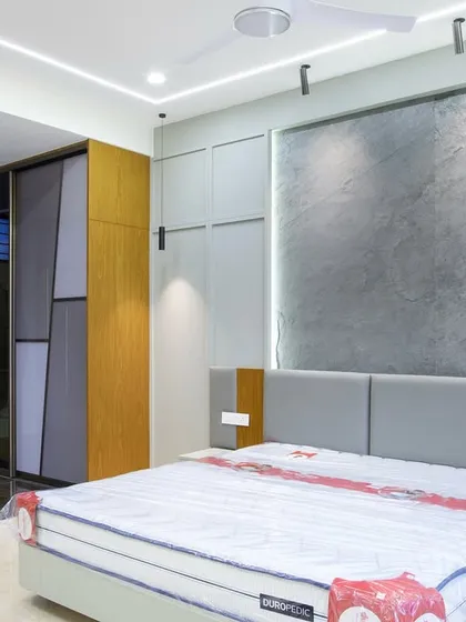 This bedroom is all about minimal surface, luxurious detail. The thin-cut granite slab behind the bed is the showstopper, framed by soft ambient lighting and custom grey paneling that conceals hidden storage.