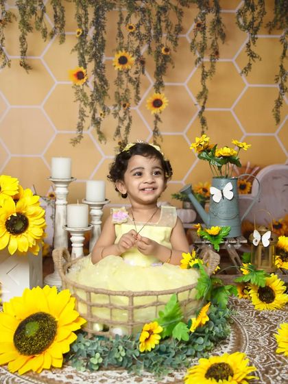 A wide shot of the cheerful sunflower theme, showing the baby in a yellow dress sitting in a basket amidst a field of flowers.