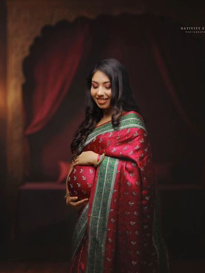 A close-up shot of the mother-to-be in a red and green saree, her expression full of joy and anticipation. The focus is on her and the baby bump.