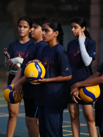 A group of our U14 girls, attentive during a coaching session, holding their volleyballs.