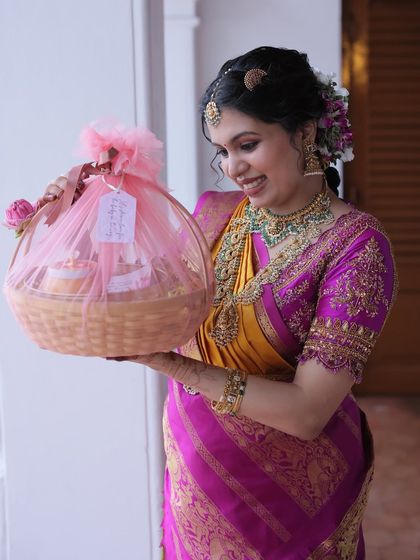 A happy client holding a fully wrapped 'Valakappu' return gift basket, adorned with pink tulle and a custom tag. It’s a beautiful way to thank guests for their blessings.