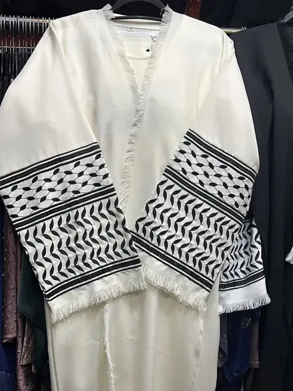 A striking white abaya with black and white patterned cuffs inspired by the keffiyeh design. The frayed edges add a modern touch to this unique piece.