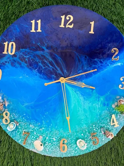 An ocean clock with Arabic numerals and a vibrant blue sea. The shore is decorated with real shells and moss for a natural look.