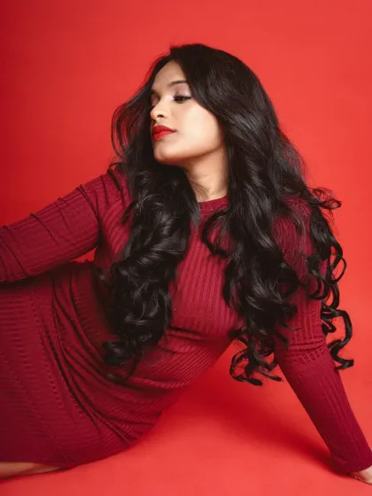 A classic portrait against a red background. The model is captured in profile, with soft lighting highlighting her features and the rich texture of her hair.