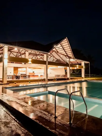 The main building and swimming pool of a delightful hostel in Chikmagalur, lit up at night for a relaxing evening swim.