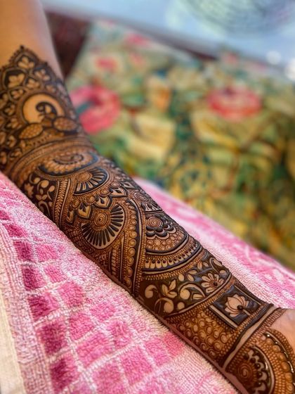 A full arm bridal mehandi design. This piece goes almost up to the elbow, featuring a large peacock, mandalas, and various traditional bands.