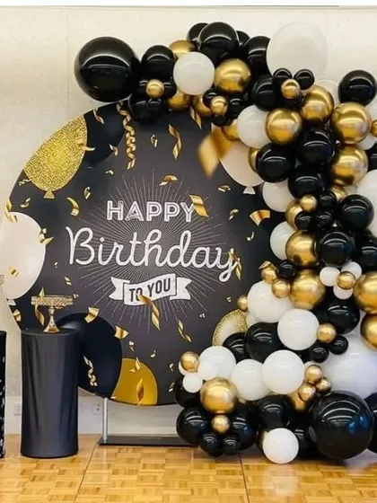 An elegant birthday backdrop with a custom printed circular panel and a balloon garland in black, white, and gold.
