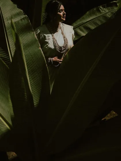 A beautiful portrait of the bride framed by giant leaves. The play of light and shadow highlights her serene expression and traditional attire during the Haldi ceremony.