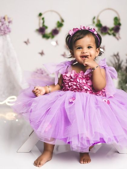 A happy one-year-old girl in a beautiful purple dress, celebrating her birthday with a butterfly and floral theme.