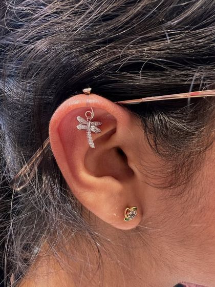 This industrial piercing is adorned with a delicate, sparkling dragonfly charm. It's a beautiful way to add a touch of nature and whimsy to an edgier piercing.