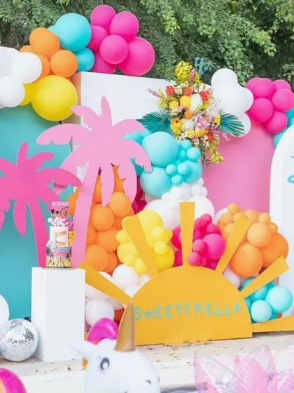 Bring on the summer vibes with a bright and tropical party theme. This incredibly colorful outdoor setup is bursting with energy, featuring hot pink palm trees, a cheerful sun cutout, and balloons in every color of the rainbow.
