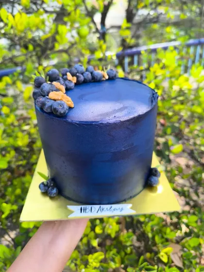 Blueberry bliss. A tall, elegant cake with a deep blue, textured buttercream finish, topped with a crescent of fresh, juicy blueberries.
