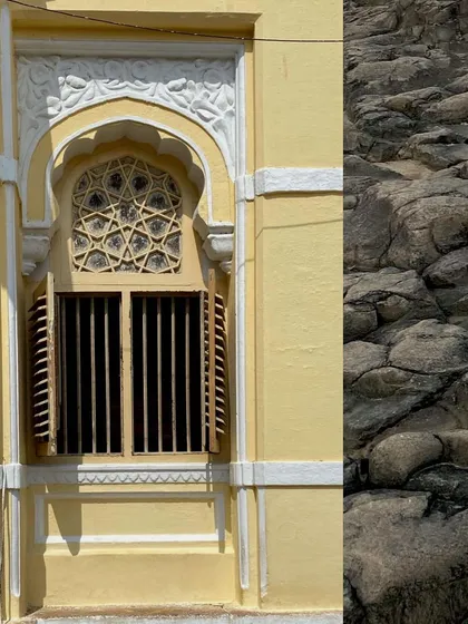 An ornate window on a yellow heritage building, next to a textured rock wall.