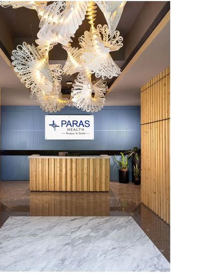 The reception at Paras Healthcare makes a powerful first impression with the 'Spiral of Life' origami chandelier. The desk and wall panels are made of fluted wood, adding warmth and texture to the entrance.