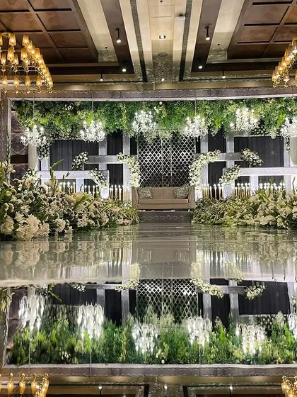 A luxury reception stage with a mirrored floor that reflects the stunning all-white floral decor and chandeliers, doubling the glamour.