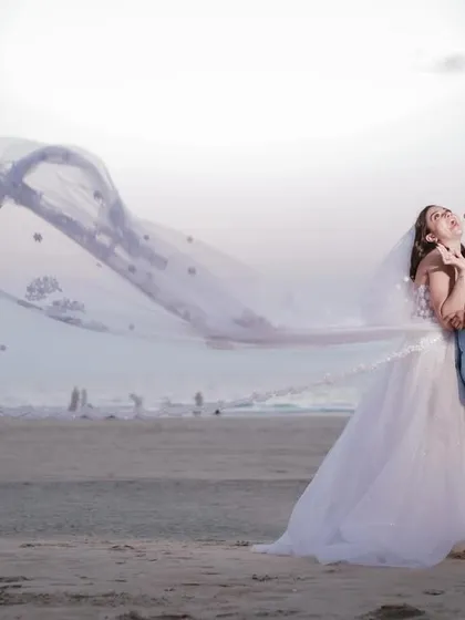 A classic, dramatic beach portrait. We used the sea breeze to catch the bride's long, embroidered veil, creating a sense of movement and fairytale elegance against the evening sky. This is a timeless wedding portrait.